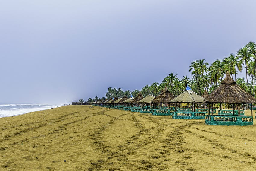 Una larga playa de arena dorada, bordeada de casetas de playa, se extiende en la distancia
